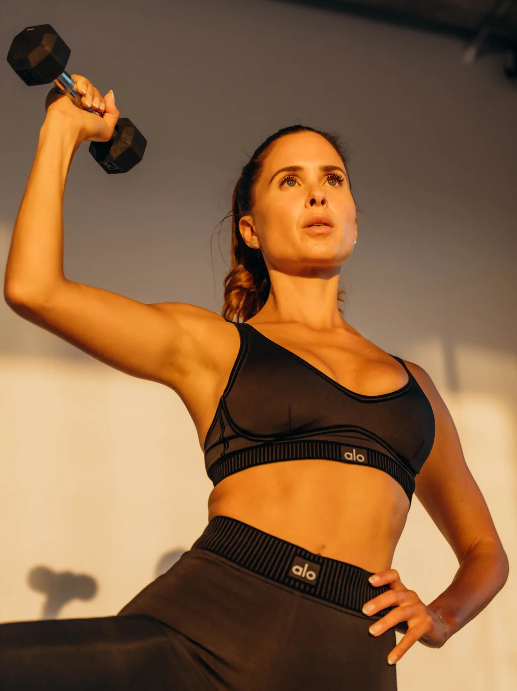 Kelsey Rose pressing a dumbbell in black activewear