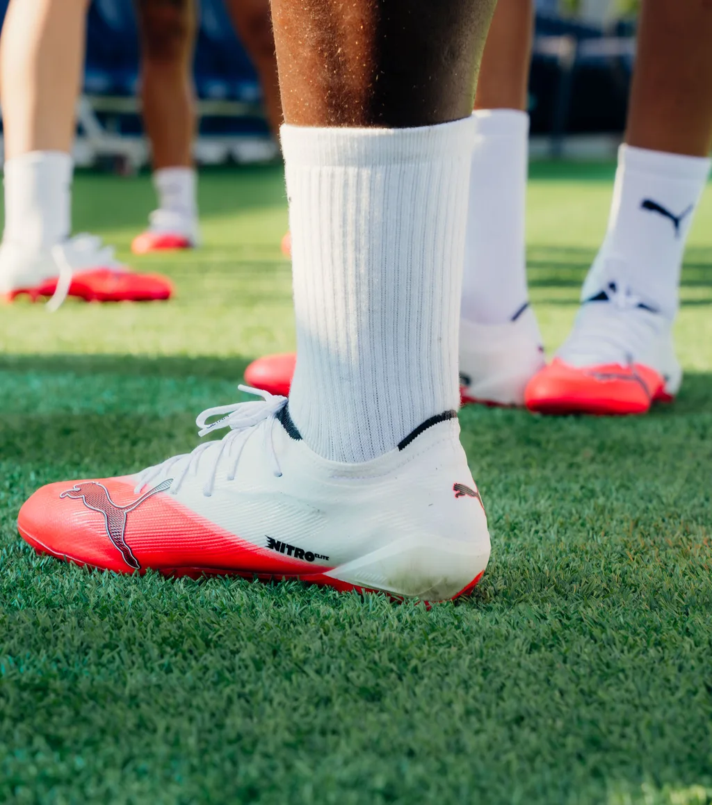 Close-up of a white and pink PUMA FUTURE boot on grass