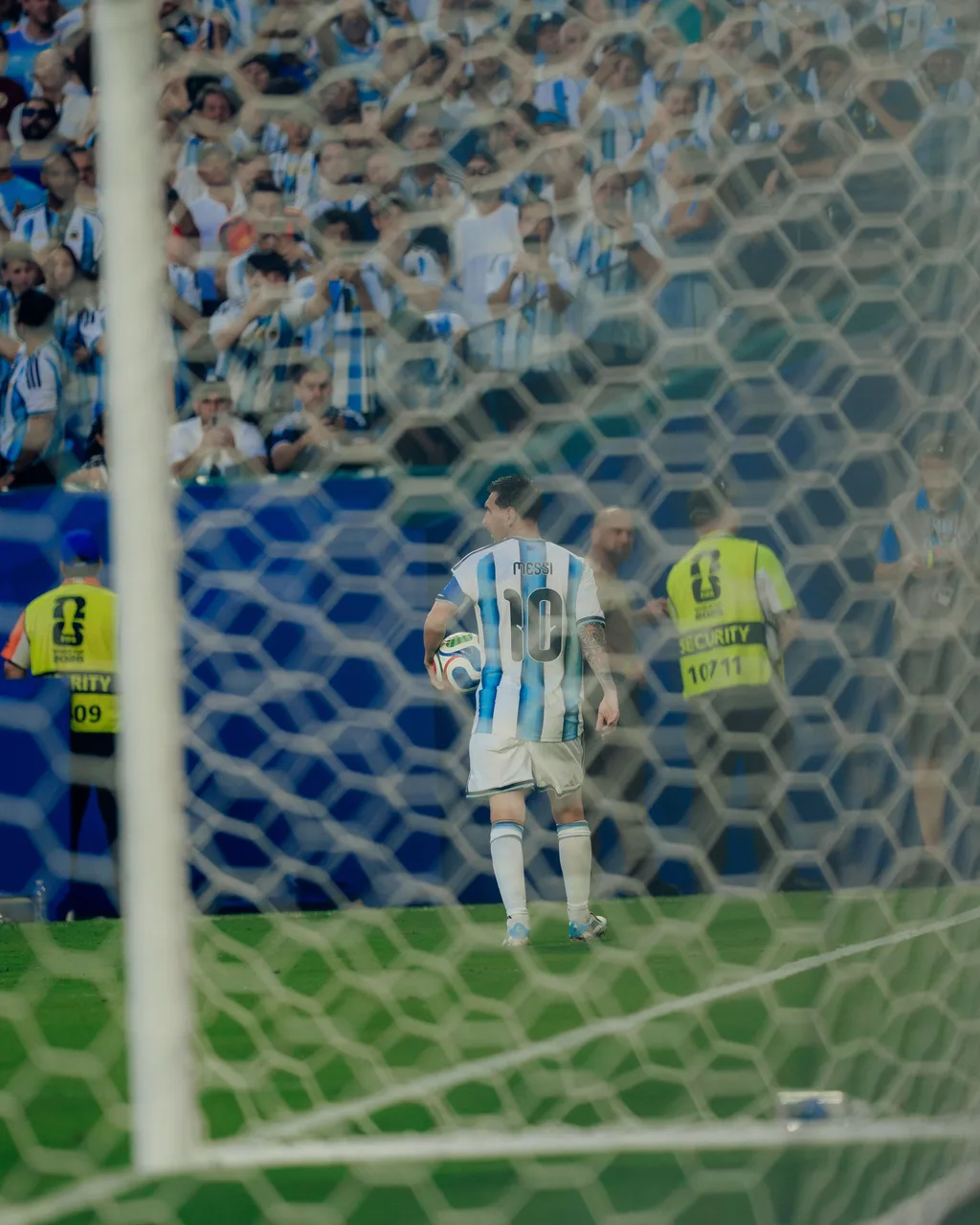 Lionel Messi seen through the goal net, ball in hand