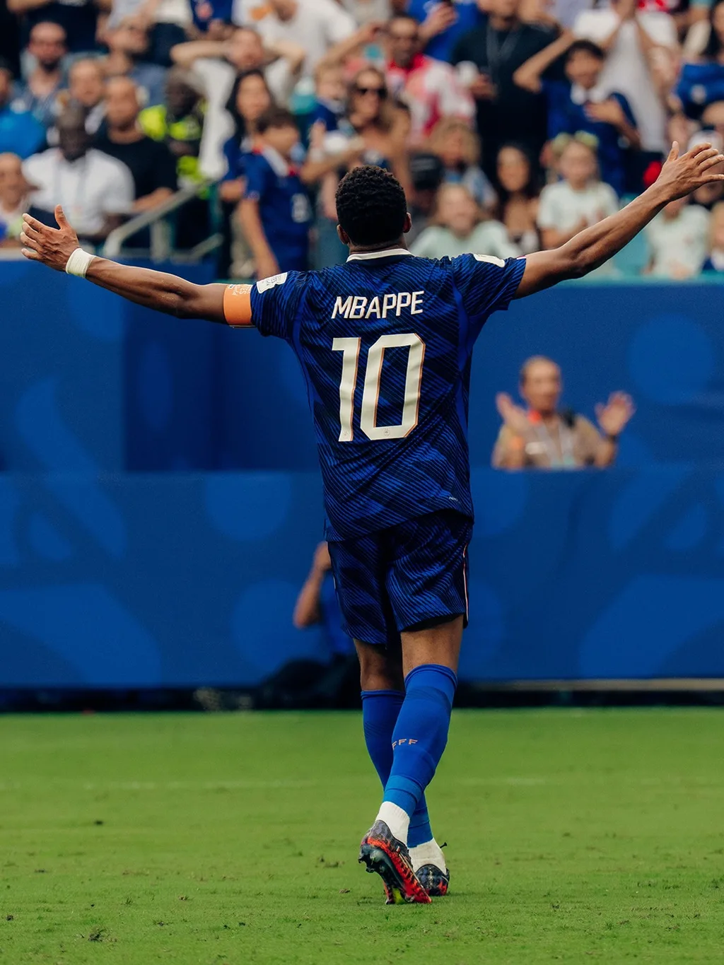 Kylian Mbappé from behind, arms spread toward the crowd